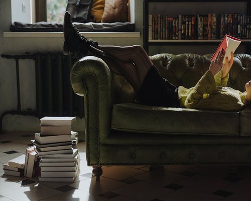 A person reading a book on a sofa near a large window